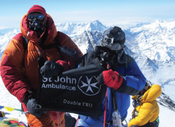 Company flag at the top of mount everest with St John Ambulance